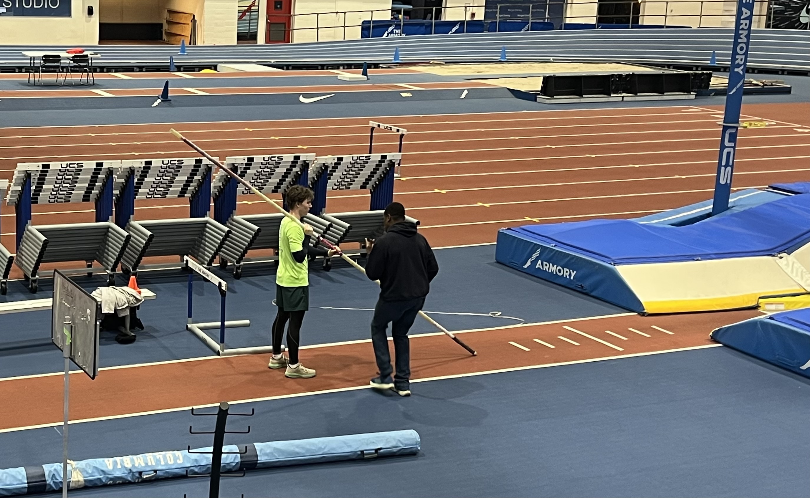 Carrying a vaulting pole along the runway beside the pole vault pit at an indoor track meet at The Armory